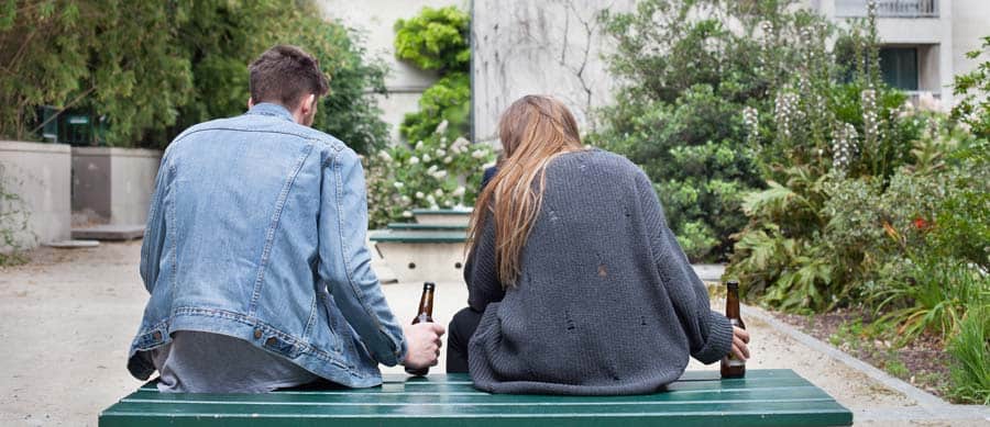 2 young people drink alcohol on a bench